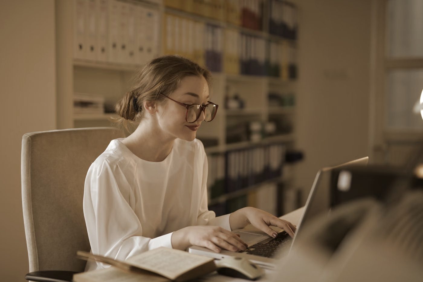 An office worker at a laptop with rows of files behind her