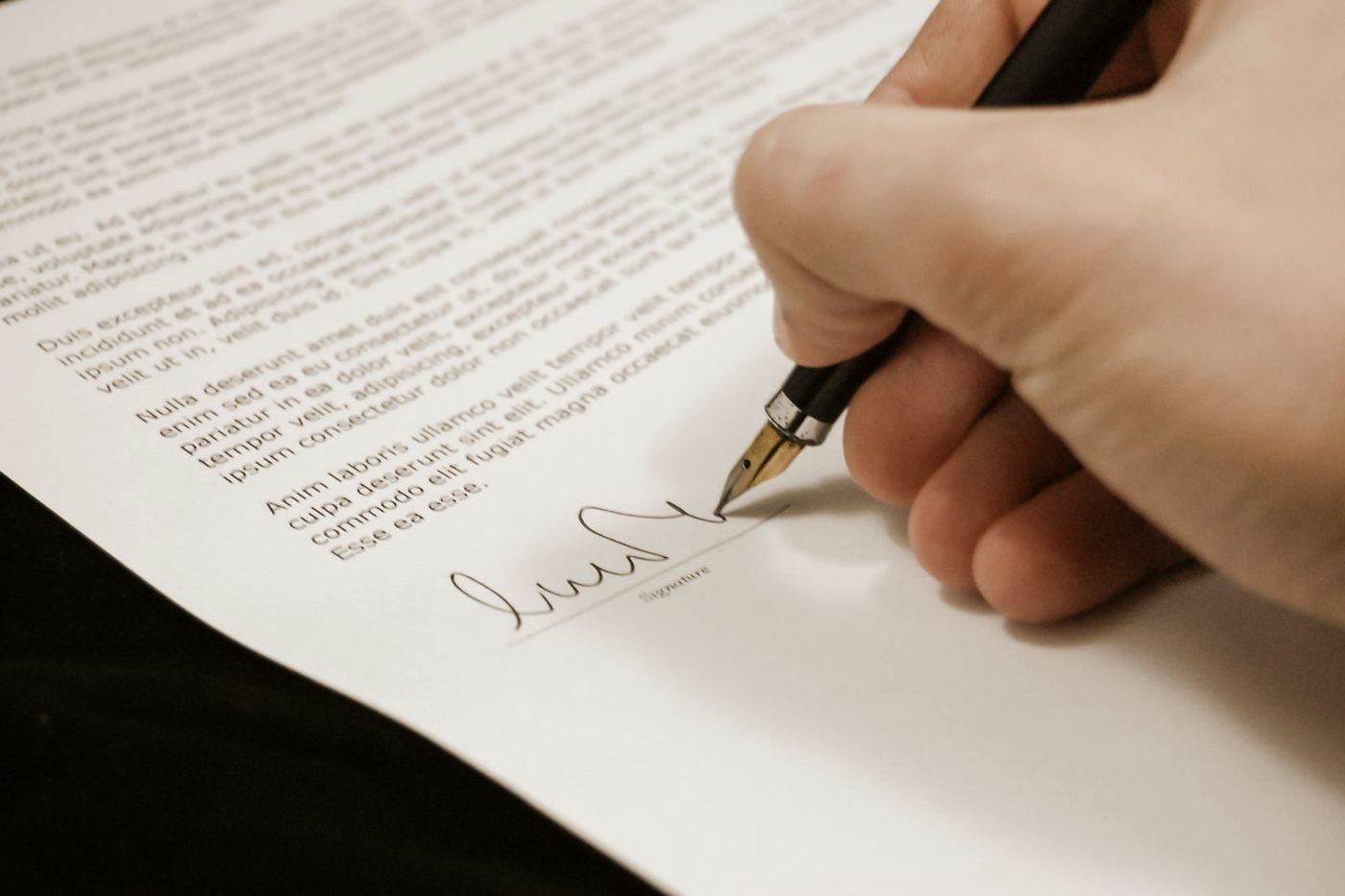 A hand signing a printed document with a fountain pen