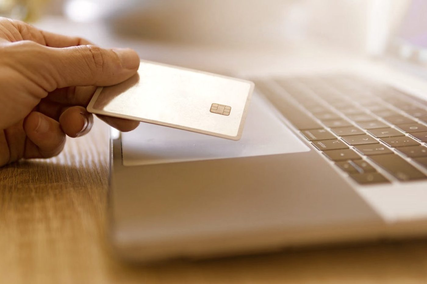 A hand holding a payment card beside an open laptop