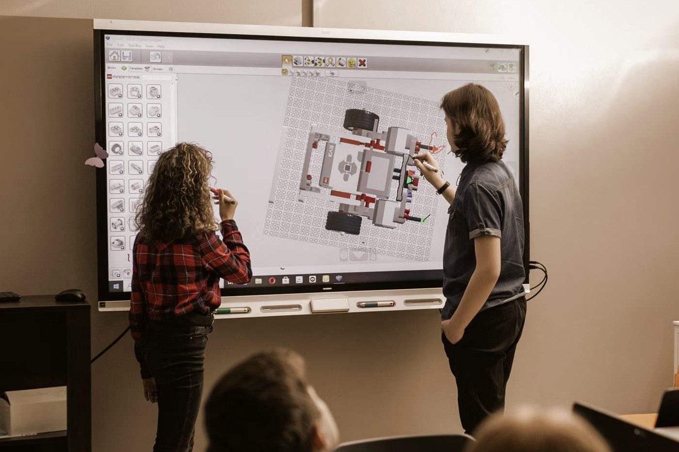 Students watching a teacher present on a large interactive touchscreen display
